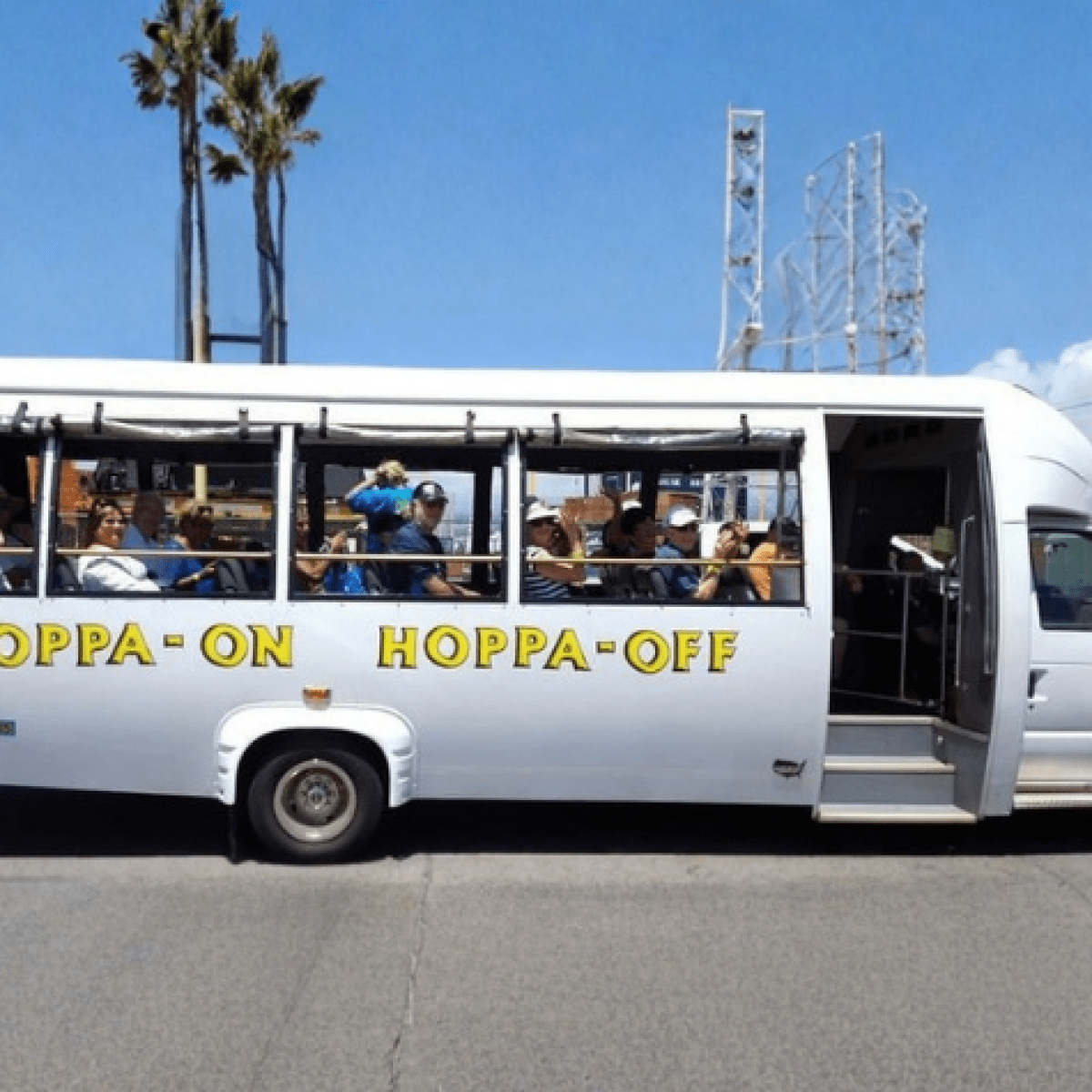 White shuttle bus with 'Kopra-OK Kopra-Off' parked in a lot with palm trees.