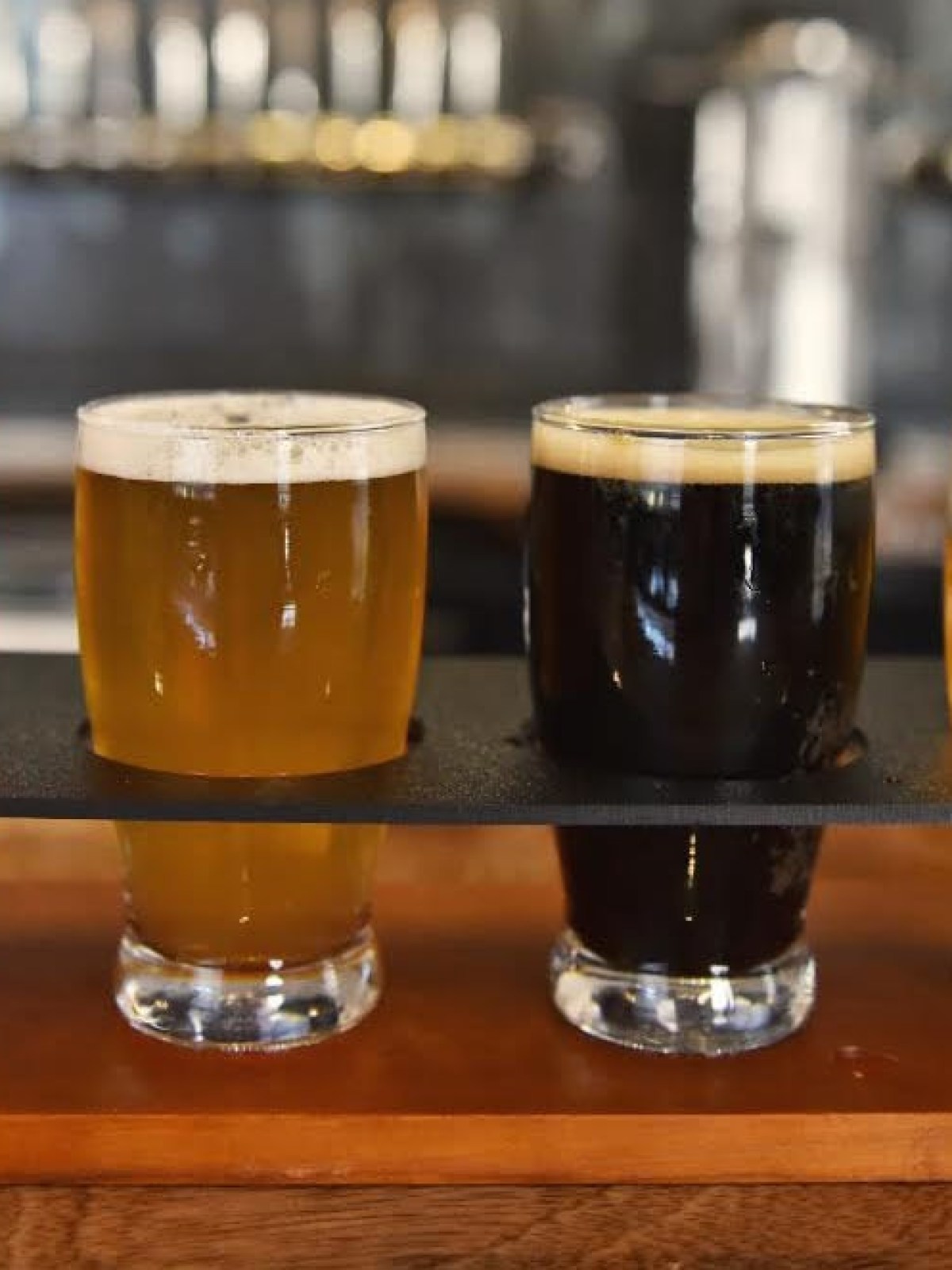 A flight of four beers with varying colors on a wooden tray at a bar.