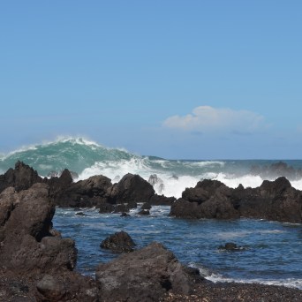 Rocky coastline with large waves under a clear blue sky.
