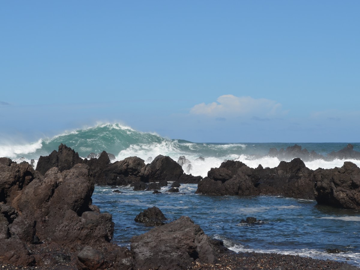 Rocky coastline with large waves under a clear blue sky.
