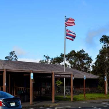 Building with two flags and parked cars in front.