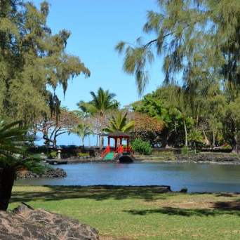Park scene with a pond, red pavilion, and trees under a clear sky.