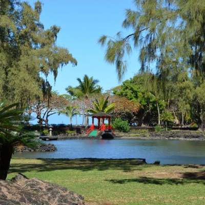 Park scene with a pond, red pavilion, and trees under a clear sky.