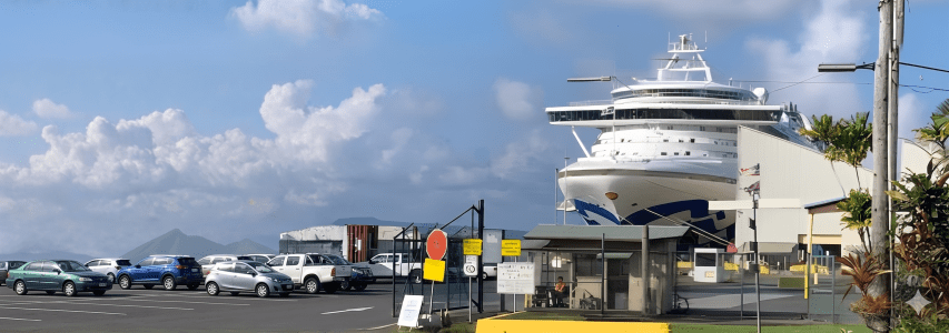 Cruise ship docked near parking lot with mountains in background.