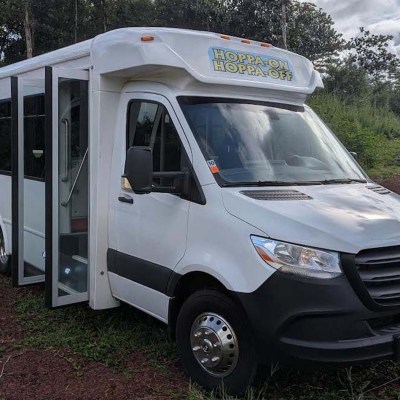 White shuttle bus with sliding door open, parked on a red gravel area.