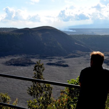 Person overlooking a volcanic crater with a mountainous backdrop.
