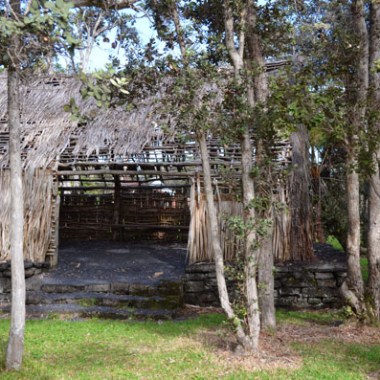 Traditional thatched hut among trees with stone base.