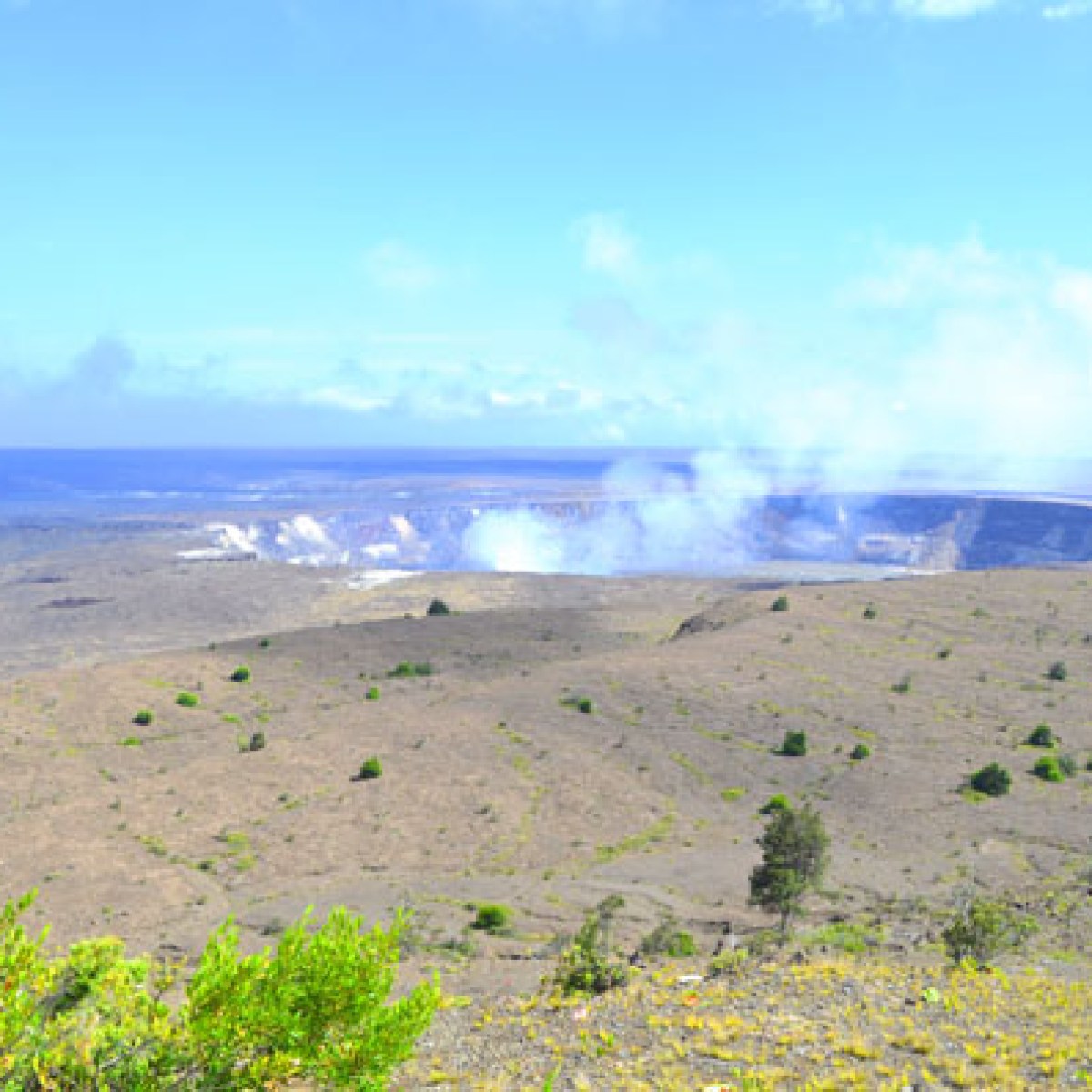 Volcanic crater with smoke under a blue sky in a barren landscape.
